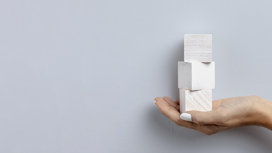 Dettaglio di una mano femminile con smalto bianco che sorregge tre blocchi di legno bianco.